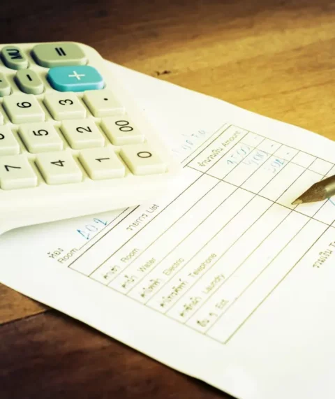 A bill and a calculator on a wooden table with a pencil on the bill.