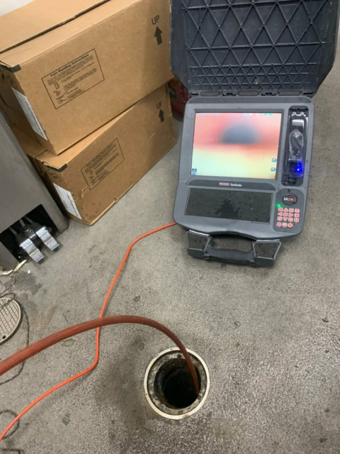 A camera inserted into a piping clean-out, or sewer pipe floor entrances, with a mobile monitor on a warehouse floor.