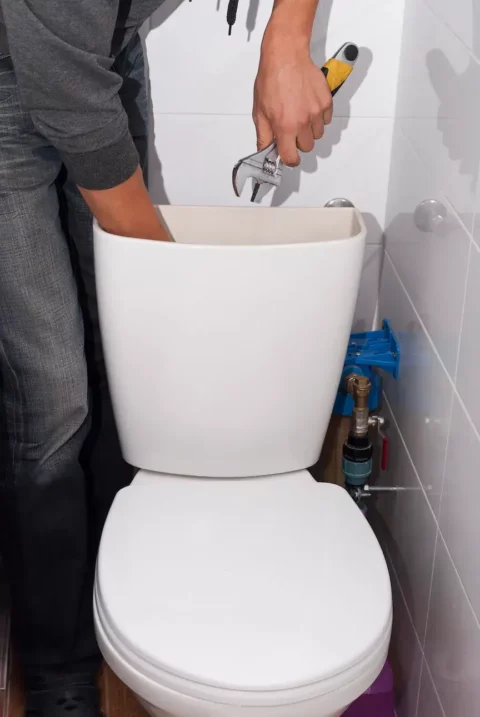 Technician repairing the inside of a white toilet with a wrench.