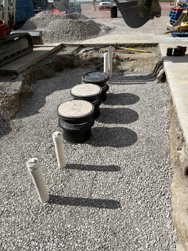Rectangular hole cut into a concrete pad backfilled with stone over new grease interceptor installation