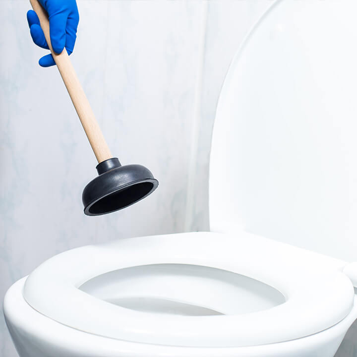 Gloved hand moving a plunger down towards a toilet