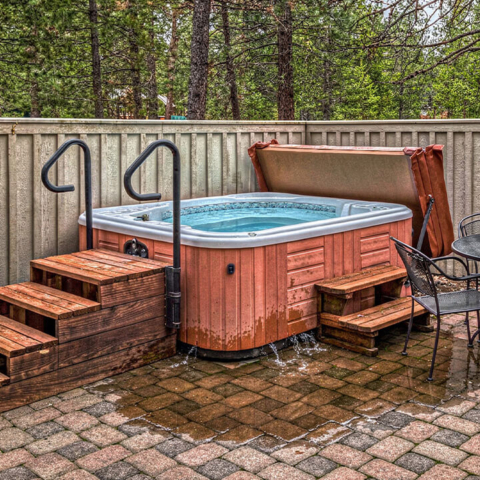 Hot tub in a backyard patio with water leaking out the base and forming a large puddle on the ground