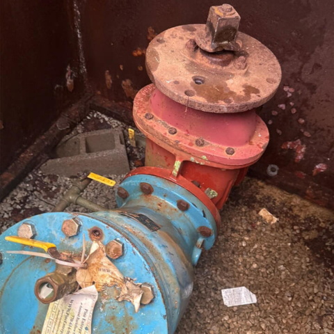 Backflows-preventer Assembly in a square vault in the ground. The valve assembly is large and is half blue painted metal and half red.