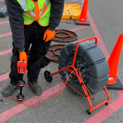 A professional plumber uses advanced pipe locating equipment and a sewer camera reel to precisely identify and map underground line issues.