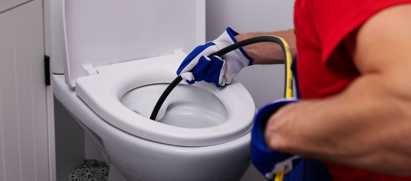 A professional plumber uses a specialized hydro-jetting hose to clear a severe blockage in a residential toilet, showcasing expert drain cleaning services.