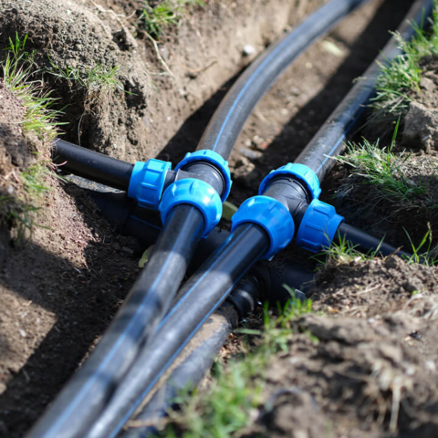 A network of underground irrigation supply lines with professional blue compression fittings in a trench, showcasing expert outdoor plumbing and main line repair services.