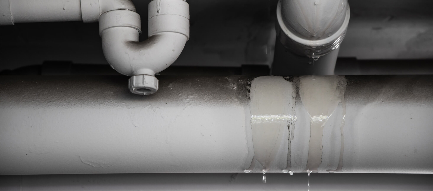 A network of PVC drainage pipes with visible water leaks and dripping joints, demonstrating the critical need for professional plumbing repair and leak detection services.