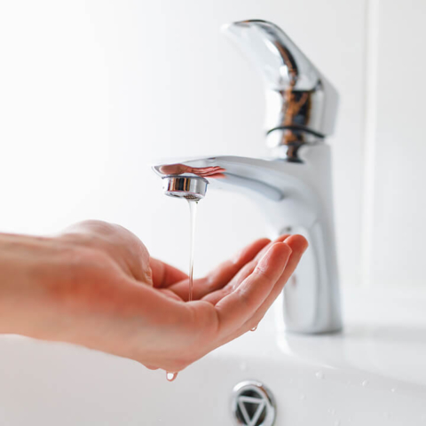 A hand under a faucet with a weak stream of water, highlighting common low water pressure problems solved by professional plumbing services.
