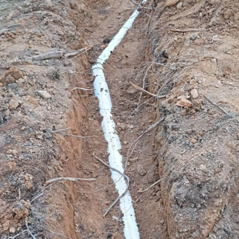 An underground installation of a new white PVC main sewer line within a professional excavation trench, showcasing expert sewer repair and replacement services.