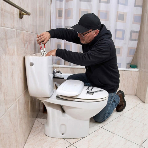 A professional plumber uses specialty tools to install or repair a residential toilet tank, showcasing expert bathroom plumbing and fixture installation services.