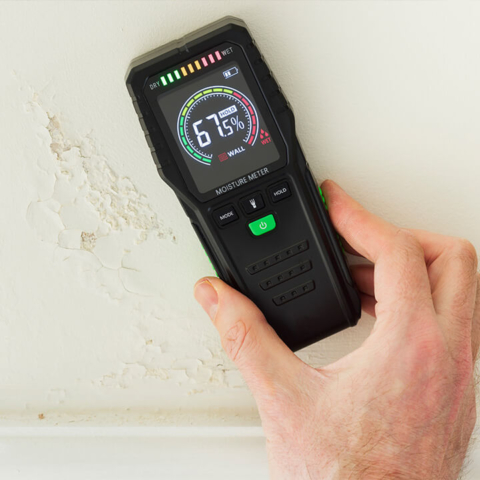 A digital moisture meter used on a water-damaged wall to pinpoint hidden leaks, representing advanced diagnostic plumbing and leak detection services.