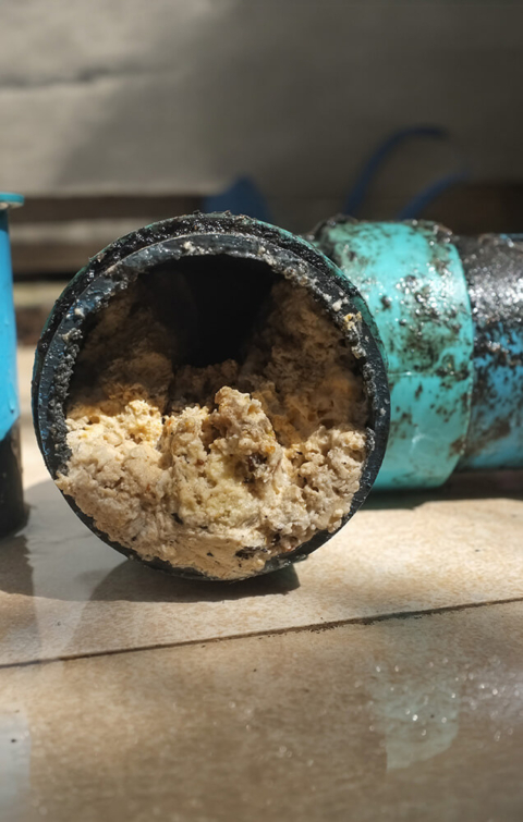 A cross-section of a drain pipe severely obstructed by thick grease and debris buildup, illustrating the critical need for professional hydro-jetting and drain cleaning services.