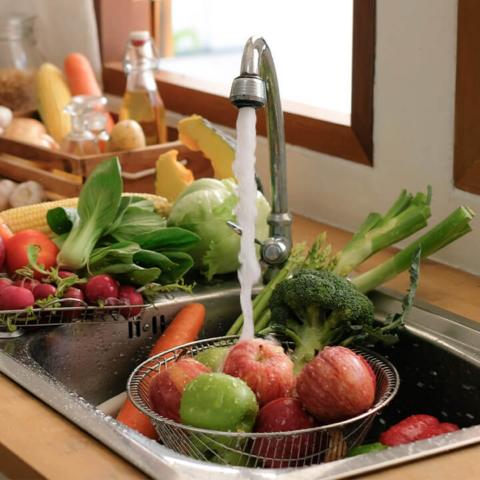 Fresh produce being washed under a high-pressure kitchen faucet, highlighting the importance of clean water and functional kitchen plumbing for a healthy home.