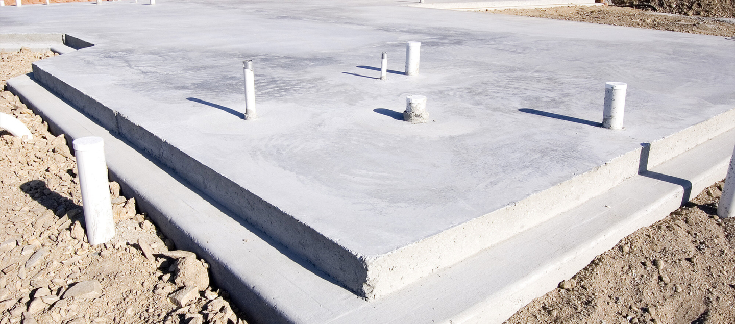A professional concrete slab foundation with white PVC plumbing stub-outs, highlighting expert rough-in plumbing services for residential new construction.