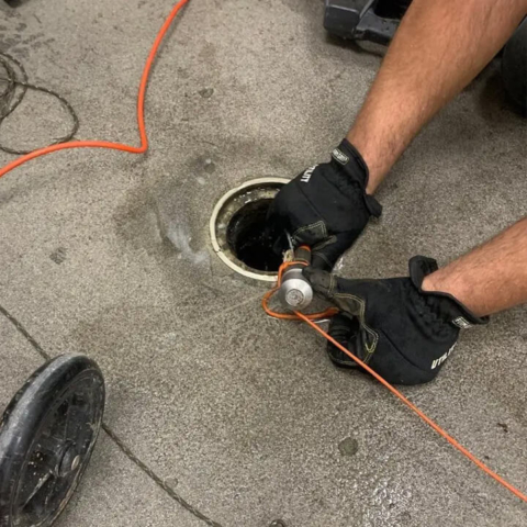 A plumbing technician carefully feeds a high-resolution televising camera into a drain to perform a detailed internal inspection of the sewer system.