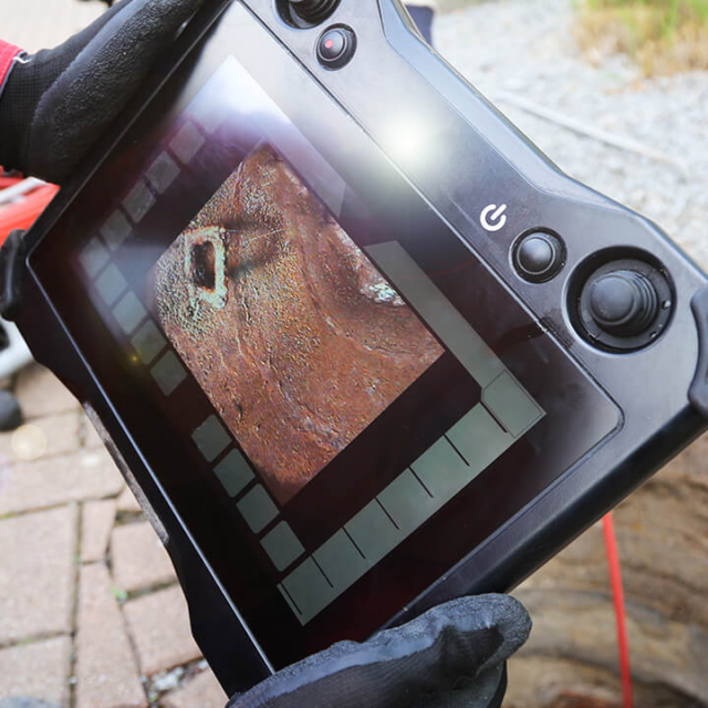 A close-up of a handheld monitor displaying live video from a sewer camera inspection, providing professional diagnostic documentation for residential and commercial plumbing repairs.