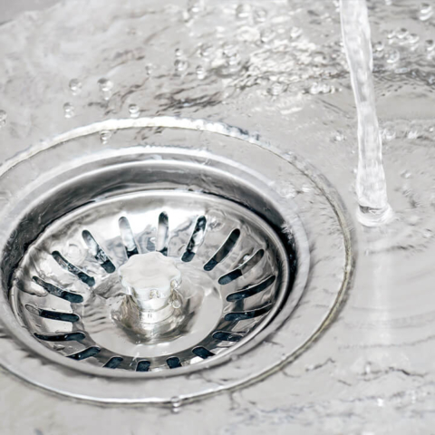 A close-up of a stainless steel kitchen sink with water flowing smoothly into the drain, showcasing efficient drainage and professional kitchen plumbing services.